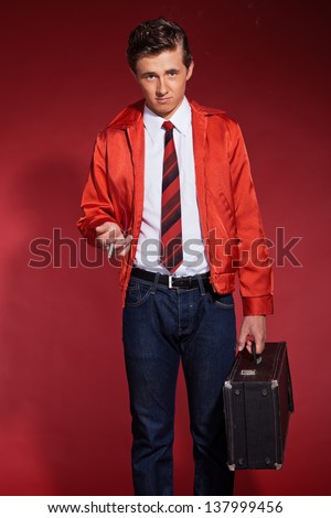 Retro fifties fashion man wearing red jacket and jeans. Holding a case and smoking.