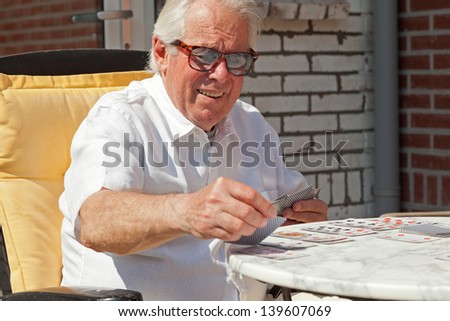 Senior man playing card game outdoor in garden.