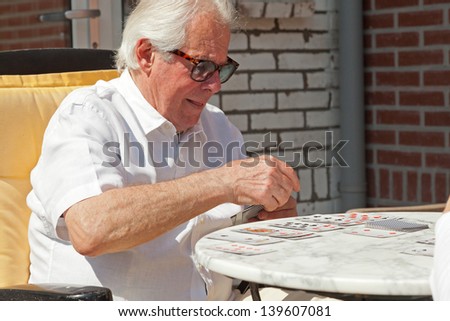 Senior man playing card game outdoor in garden.