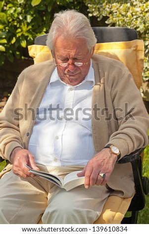 Senior man reading a book in garden in summer.
