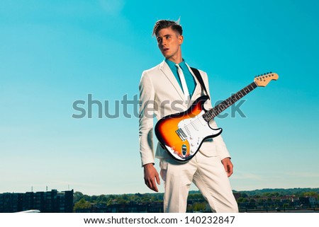 Vintage 50s male electric guitar player with white suit. On rooftop. Blue sky.