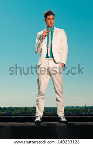 Retro summer 50s fashion man with white suit. Holding sunglasses. On rooftop. Blue sky.