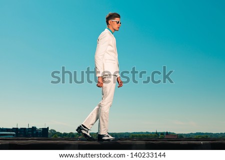 Retro fifties summer fashion man with white suit and sunglasses. On rooftop. Blue sky.