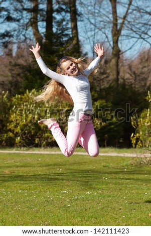 Blonde girl jumping on field of grass in park.