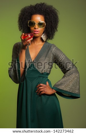 Retro 70s afro fashion woman with green dress and orange cocktail glass. Green background.
