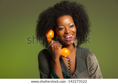 Retro 70s afro fashion woman with green dress. Calling with orange phone. Green wall.