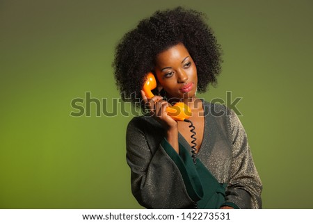 Retro 70s afro fashion woman with green dress. Calling with orange phone. Green wall.