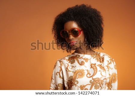 Retro 70s fashion african woman with paisley dress and sunglasses. Brown background.