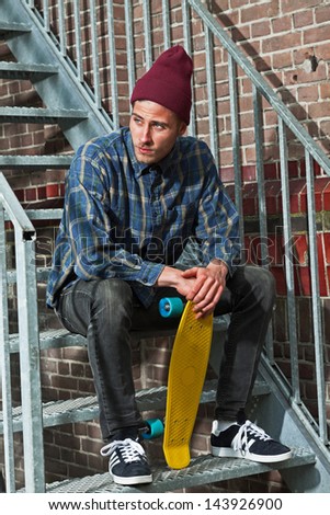 Urban skateboarder with woolen hat holding his skateboard sitting on iron stairs.