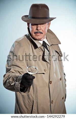 Retro detective with mustache and hat. Looking through magnifying glass. Studio shot.