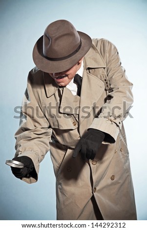 Vintage detective with mustache and hat. Looking through magnifying glass. Studio shot.