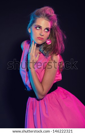 Naughty retro 80s fashion girl with pink dress and long blonde hair. Black background.