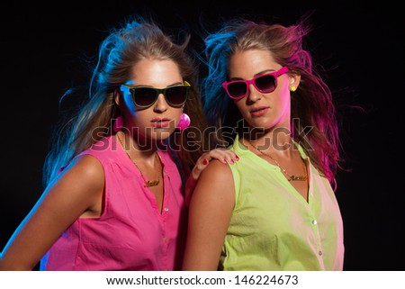 Two sexy retro 80s fashion girls with long blonde hair and sunglasses. Twin sisters together.