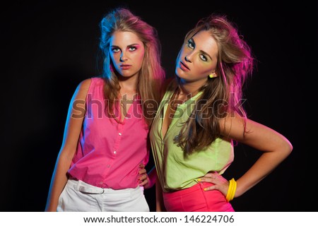 Two sexy retro 80s fashion girls with long blonde hair. Twin sisters together.