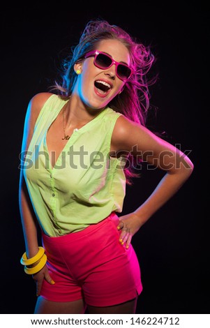 Sexy retro 80s fashion disco girl with long blonde hair and pink sunglasses. Black background.