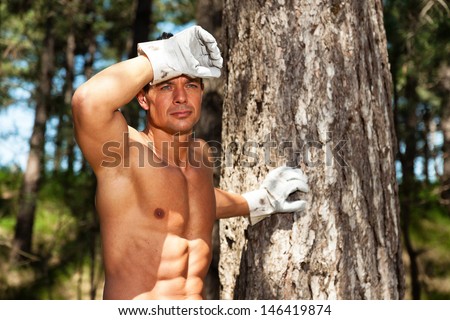 Shirtless muscled fitness man with working gloves in forest. Resting and staring.