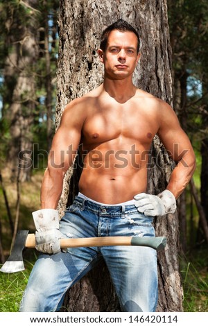 Shirtless handsome muscled lumberjack man with axe in forest.