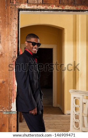 Retro fashion afro american groom wearing black suit and tie and sunglasses. Interior of old house.