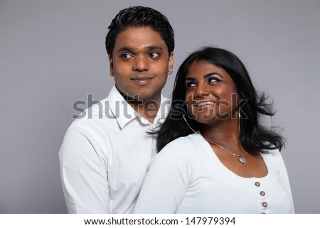 Young romantic indian couple. Wearing white shirt and jeans. Studio shot against grey.