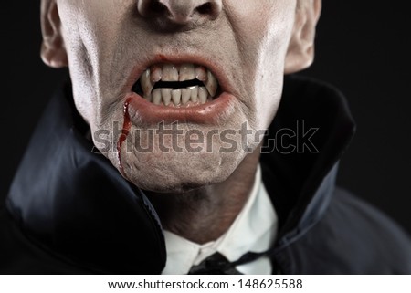 Close-up of dracula with black cape showing his scary teeth. Vamp fangs. Studio shot against black.