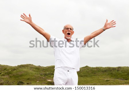 Free happy retired senior man with beard and glasses enjoying the outdoors with cloudy sky.