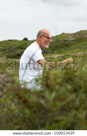 Retired man with beard and glasses resting and having lunch in grass dune landscape. Dressed in white.