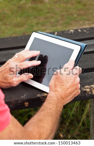 Close-up of hands of retired senior man resting and using his tablet at table in grass dune landscape.