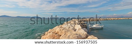 Panoramic shot of seascape with curved stone pier. Fishing boat. Blue cloudy sky.