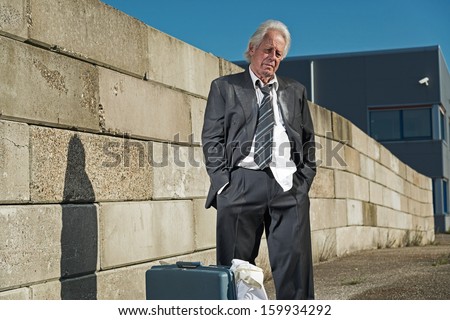 Depressed senior business man with suitcase without a job and homeless on the street. Wearing a dirty suit.