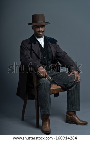 Retro afro america western cowboy man with mustache. Sitting in wooden chair holding a gun. Wearing brown hat. Cool tough guy.