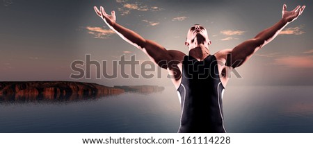 Muscled fitness triathlon athlete. Arms spread wide. Victory. Standing near lake at sunset.