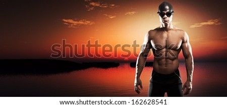 Muscled swimmer man with cap and glasses outdoor at a lake at sunset. Extreme fitness sport.