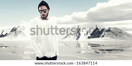 Cool man with beard in winter fashion. Wearing white woolen sweater black cap and sunglasses. Outdoor in snow mountain landscape.