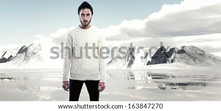 Cool man with beard in winter fashion. Wearing white woolen sweater and black cap. Outdoor in snow mountain landscape.