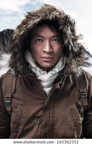 Asian Winter Sport Fashion Man With Backpack In Snow Mountain Landscape. Wearing Brown Jacket With Fur Hoody.