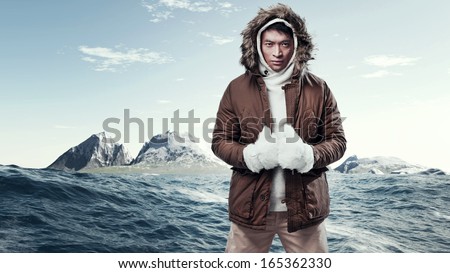 Asian Winter Sport Fashion Man In Arctic Mountain Landscape. Wearing Brown Jacket With Fur Hoody And White Gloves.