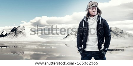Asian Winter Fashion Man In Snow Mountain Landscape. Wearing Black Jacket With Furry Hat And Gloves.