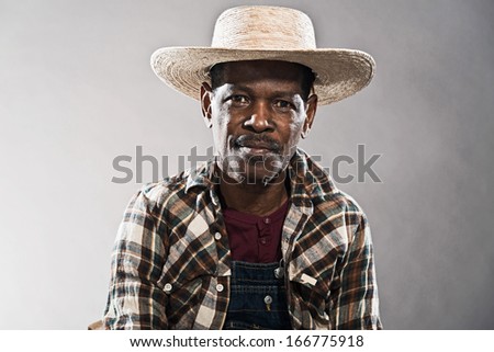 Retro senior afro american blues man in times of slavery. Wearing denim bib and brace overall with straw hat.