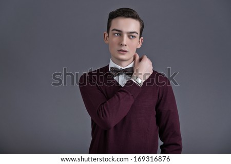 Retro fifties english style fashion young man. Wearing dark red shirt and bow tie. Studio shot against grey.