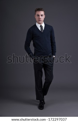 Retro fifties style fashion young man. Wearing dark blue shirt and tie. Studio shot against grey.
