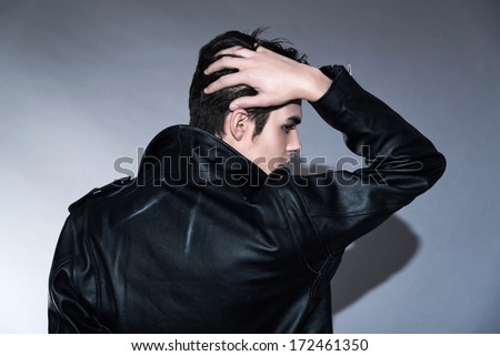 Cool retro rock and roll 50s fashion man. Hand in his hair. Wearing black leather jacket. Studio shot against grey.