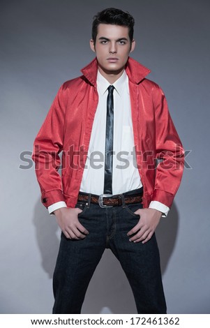 Retro rock and roll fifties fashion man with dark grease hair. Wearing red jacket and jeans. Studio shot against grey.