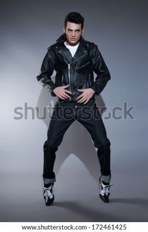 Retro rock and roll 50s fashion man with dark grease hair. Wearing black leather jacket and jeans. Studio shot against grey.