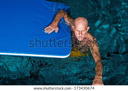 Healthy active senior man with beard in indoor swimming pool playing with foam raft.