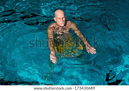 Healthy active senior man with beard in indoor swimming pool. Wearing yellow swimming trunks.