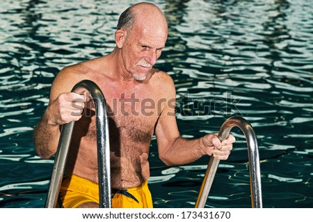 Senior man walking out of swimming pool. Wearing yellow swimming trunks.