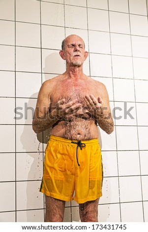 Senior man taking a shower in bathroom. Wearing yellow swimming trunks.