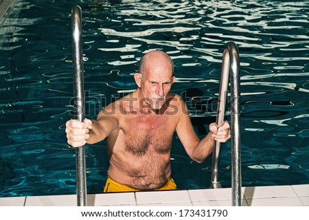 Senior man walking out of swimming pool. Wearing yellow swimming trunks.