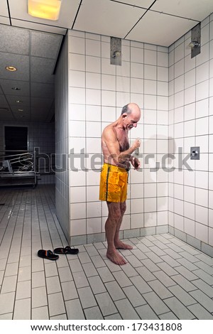Senior man taking a shower in bathroom. Wearing yellow swimming trunks.