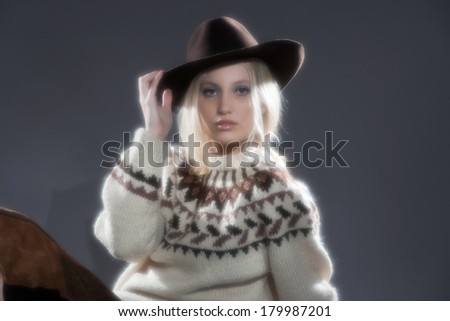 Retro soft focus hippie 70s winter fashion girl with long blonde hair. Wearing a hat. Studio shot against grey.